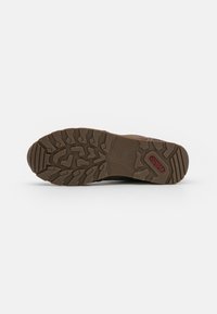 Brown rubber shoe sole with multi-directional tread pattern, featuring a circular logo and textured areas for traction.