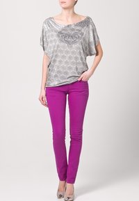 Top suelto de color gris metálico con diseño estampado, combinado con jeans ajustados de un brillante color púrpura y zapatos de color neutro.