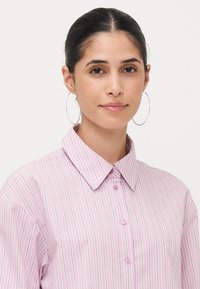 Pink striped button-up shirt with a collar. The fabric features vertical pinstripes in varying pastel colors and a smooth texture.
