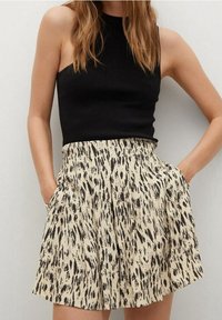 Black sleeveless top paired with a beige pleated skirt featuring a black animal print pattern. Skirt has side pockets and a flared silhouette.