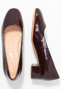 Talons en cuir verni bordeaux avec un bout carré et un talon large, dotés d'une semelle intérieure rembourrée avec des perforations pour la ventilation.