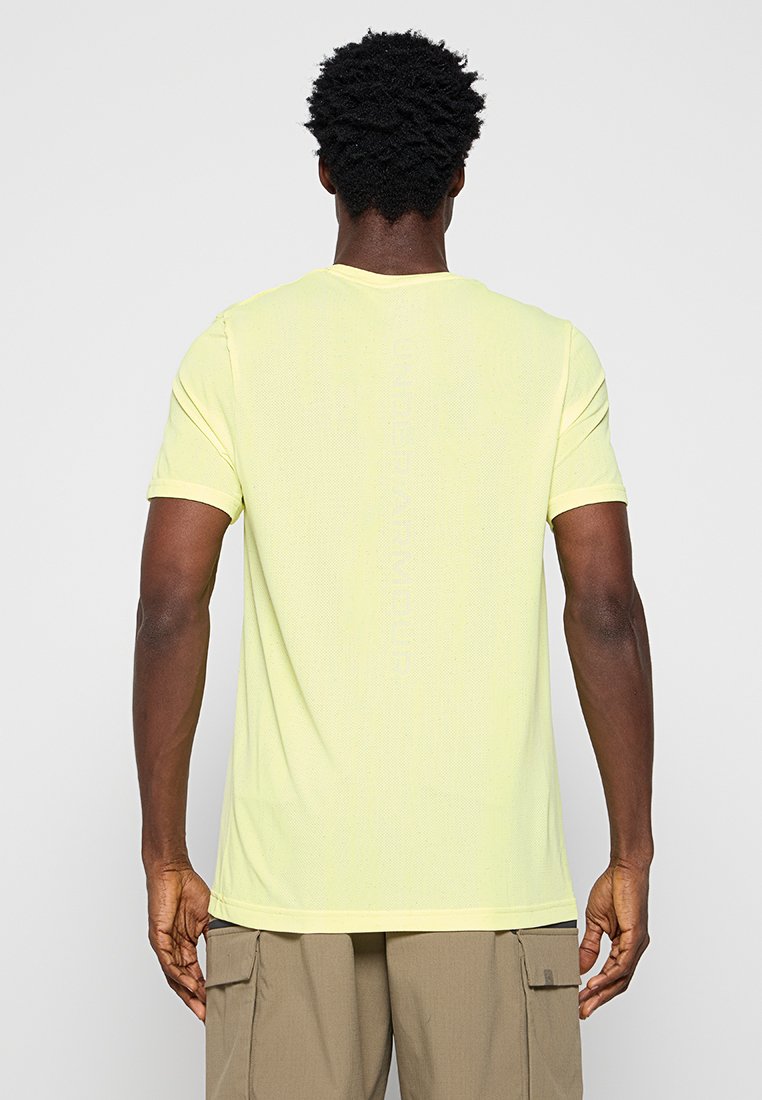 T-shirt giallo chiaro a maniche corte con scollatura rotonda, realizzato in tessuto textured. Presenta un marchio sottile lungo la parte posteriore.