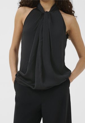 Schwarzes Neckholder-Top mit geknotetem Frontdetail, gefertigt aus einem leichten, strukturierten Stoff und mit lockerem Schnitt. Kombiniert mit schwarzen Hosen.