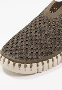 Scarpa perforata marrone con un motivo ondulato, caratterizzata da una tomaia in morbido scamosciato, suola in gomma a contrasto e cuciture visibili lungo il bordo.