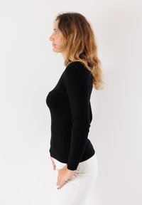 Top lungo aderente nero a coste con silhouette attillata, tessuto testurizzato e scollatura rotonda, abbinato a pantaloni bianchi.