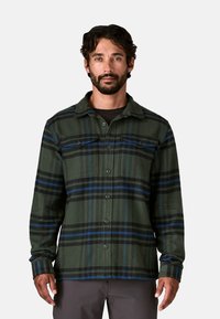 Camicia in flanella verde a quadri con strisce blu e nere, con chiusura a bottoni, colletto e due tasche sul petto, realizzata in tessuto morbido.