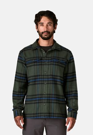 Camicia in flanella verde a quadri con strisce blu e nere, con chiusura a bottoni, colletto e due tasche sul petto, realizzata in tessuto morbido.