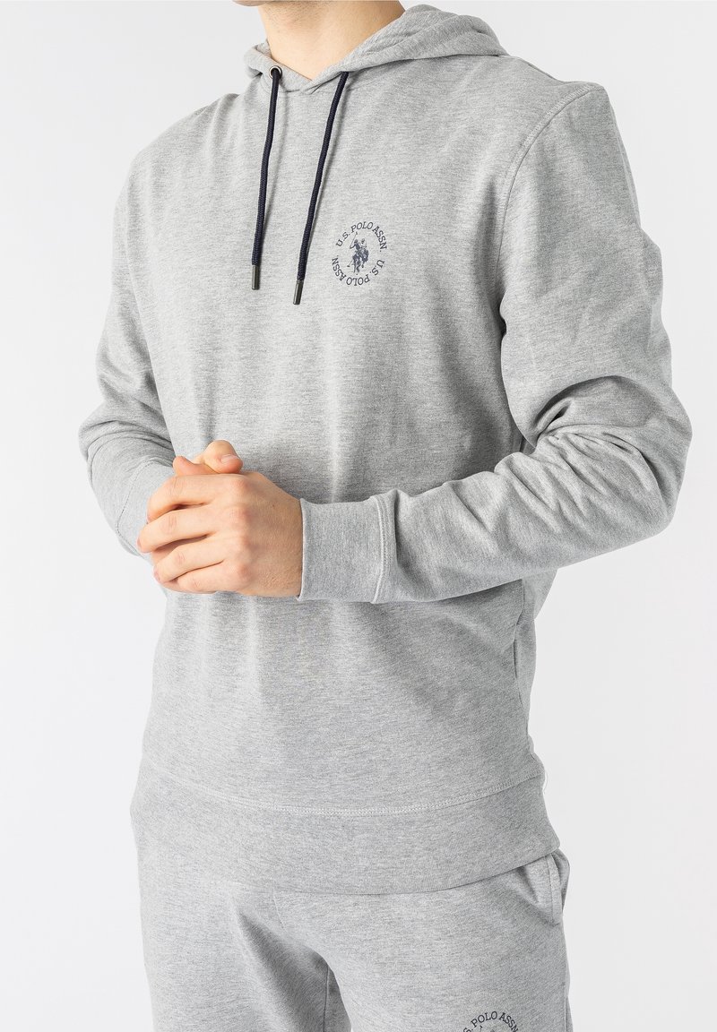 Grå hoodie med dragsko och framsidan logotyp. Tillverkad av mjukt material, har ribbade mudd och en känguruficka. Lätt design.