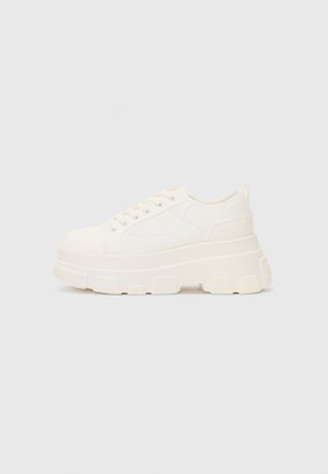 Fehér vászon sportcipő vastag talppal, lekerekített orral és öt fűzőlyukkal. Hátulján egy fül a könnyű felvétel érdekében. Simára kidolgozott textúra, minimális dizájn.