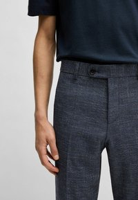 Navy blue tailored trousers with a textured fabric, featuring a button closure, side pockets, and a slim fit. No visible patterns or graphics.