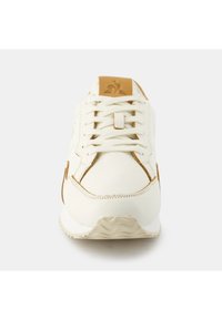 Sneaker bianca con accenti in suede marrone, suola testurizzata, punta rotonda e design classico con lacci. Il logo beige sulla linguetta esalta i dettagli.