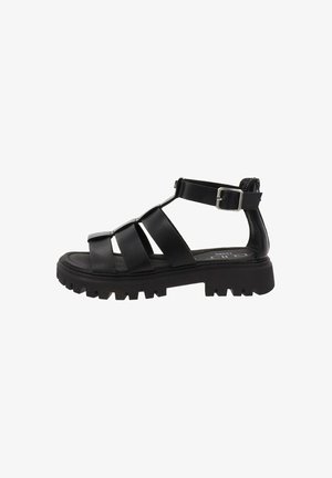 Sandalias negras con tiras y suela gruesa, parte superior de cuero, hebilla ajustable en el tobillo y suela rugosa para tracción. Diseño plano y detalle de hebilla sencillo.