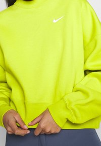 Neon gul sweatshirt med ribbad rundhals, långa ärmar och en vit Nike-logotyp på bröstet. Mjukt tyg med en avslappnad passform.