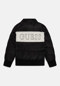 Kurtka puchowa w kolorze czarno-białym. Posiada poziomy biały panel z logo "GUESS". Pikowany wzór, ściągacze na rękawach i u dołu kurtki.