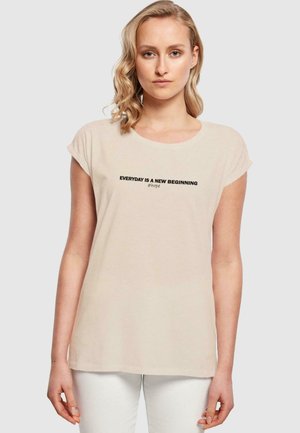 Beige Baumwoll-T-Shirt mit kurzen umgeschlagenen Ärmeln, Rundhals und schwarzem Text "JEDER TAG IST EIN NEUER BEGINN #Hoffnung" auf der Brust.