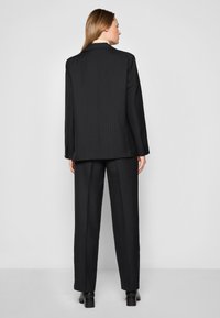 Svart dressjakke og bukser med pinstriper, som har en avslappet passform og glatt tekstur, med en enkelt knappelukking på jakken.