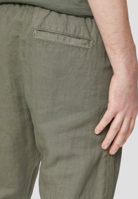 Oliwkowe lniane spodnie o teksturowanej powierzchni, z elastycznym pasem i tylną kieszenią z subtelnymi detalami przeszycia.