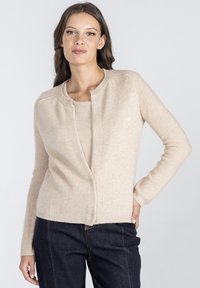 Beżowy kardigan z okrągłym dekoltem, długimi rękawami i miękką teksturą. Posiada zapięcie z przodu oraz ribbowe detale u dołu.