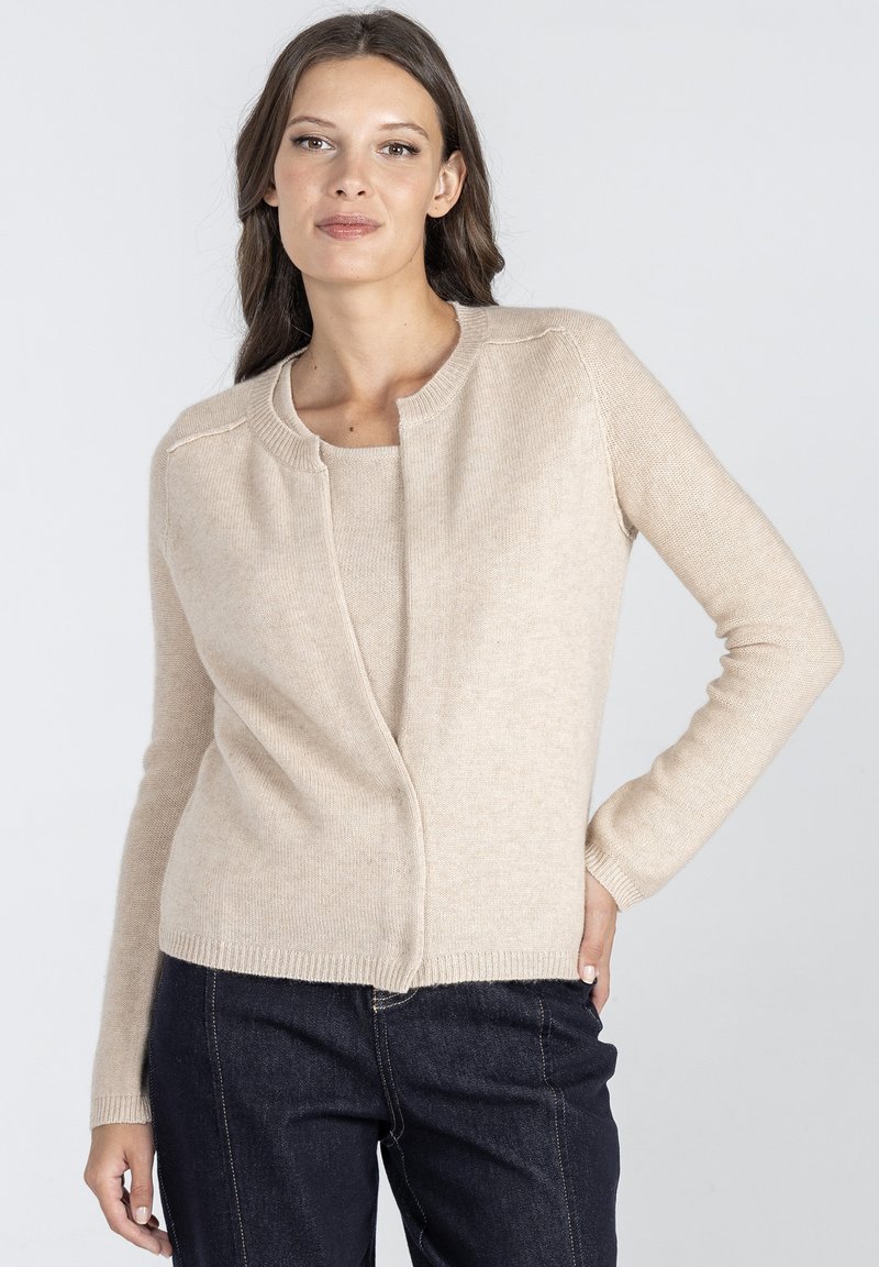 Beżowy kardigan z okrągłym dekoltem, długimi rękawami i miękką teksturą. Posiada zapięcie z przodu oraz ribbowe detale u dołu.