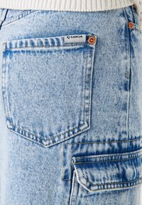 Jean en denim bleu clair avec un design classique à cinq poches, des coutures contrastantes et une petite étiquette de marque sur la poche arrière.