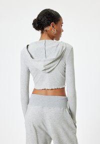 Grijze crop hoodie met lange mouwen en een capuchon. Ribbelstructuur, onafgewerkte zoom en een naaddetail langs de achterkant. Gecombineerd met bijpassende onderkleding.