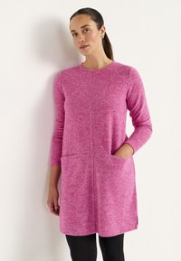 Rosa gestricktes Kleid mit langen Ärmeln, rundem Ausschnitt, zwei vorderen Taschen und seitlichen Schlitzen für zusätzliche Bewegungsfreiheit. Weicher Stoff, mittellanges Design.