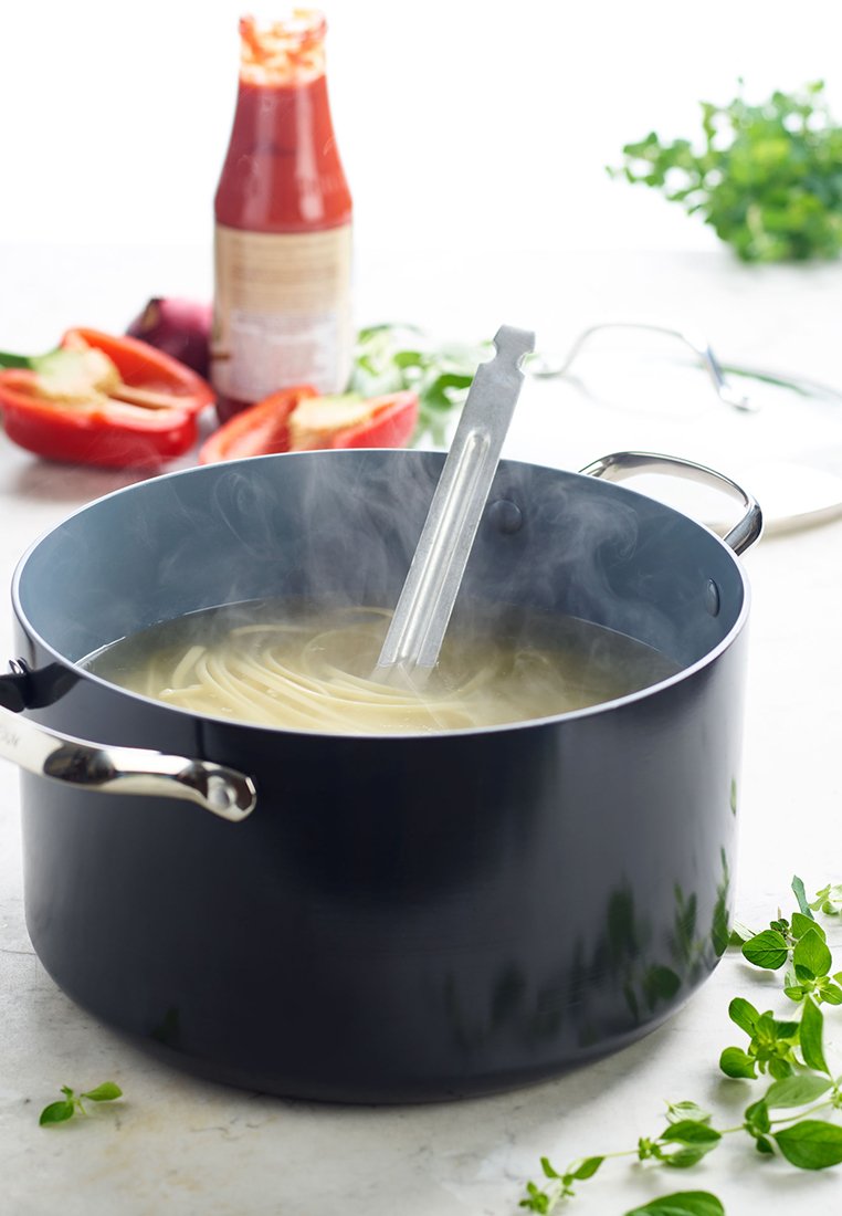 Dampfender Topf mit Spaghetti, die im Wasser kochen, und einer Pastazange darin, mit geschnittenen roten Paprika und einer Sauceflasche im Hintergrund.