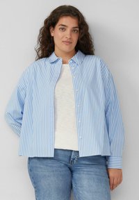 Lichtblauw en wit gestreept overhemd met een kraag en lange mouwen, gecombineerd met een wit T-shirt en blauwe jeans.