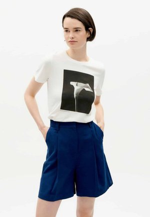 White T-shirt with a black graphic design paired with blue tailored shorts. The shorts have side pockets and a structured fit.
