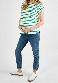 Camiseta de maternidad con rayas horizontales verdes y blancas, de manga corta, combinada con vaqueros azules y zapatillas blancas con acentos beiges.