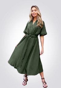 Vestido de lino verde oliva de longitud media, con mangas cortas, cuello con muesca y cintura atada. Presenta un dobladillo fluido y un ligero brillo.