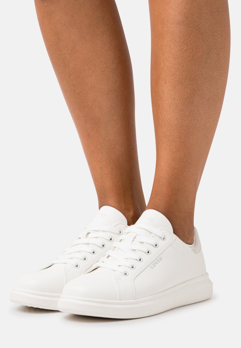 Baskets en cuir blanc avec une finition lisse, bout rond, lacets plats et un design minimaliste avec des accents gris au niveau du talon.