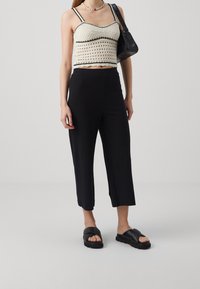 Haut blanc court avec accents noirs, pantalon noir côtelé et sandales noires. Design texturé avec une coupe ajustée et une fente à l'ourlet.