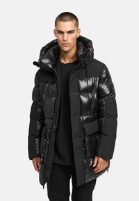 Svart puffjacka med en glänsande yta, utrustad med huva, flera fickor och dragkedjestängning. Tighta puffar ökar isoleringen.