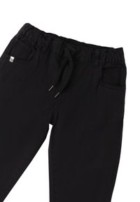 Pantalones de chándal negros hechos de tejido suave, que cuentan con una cintura elástica, cordón ajustable y bolsillos laterales. Textura suave y diseño casual.