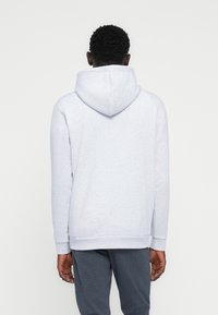 Ανοιχτό γκρι φούτερ με υφή, με μεγάλο κουκούλα, μακριά μανίκια και ριμπ μανσέτες. Η πλάτη χαρακτηρίζεται από απλότητα στο σχέδιο.