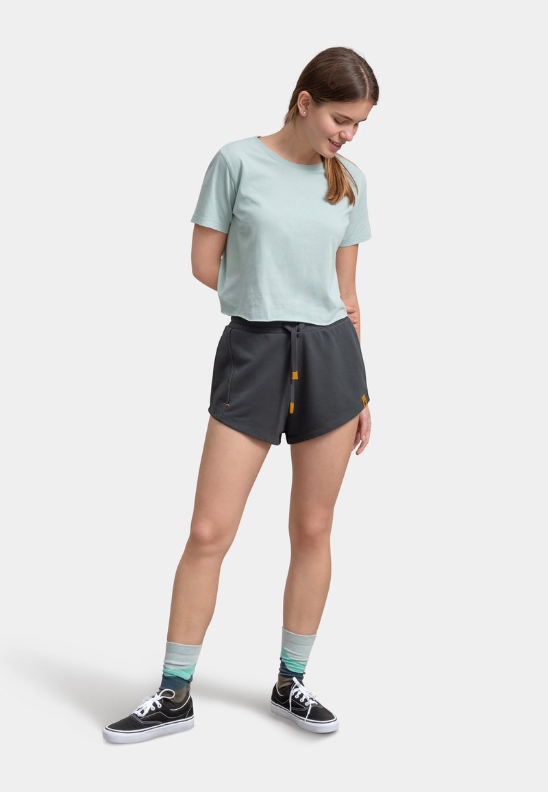 T-shirt in cotone azzurro chiaro abbinato a pantaloni corti grigio antracite. I pantaloni presentano un cordoncino e due dettagli gialli, indossati con sneakers nere e calze a fantasia.