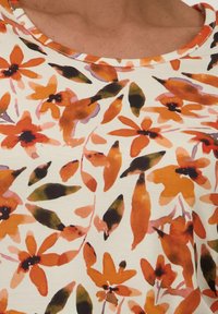 Bloemenpatroon stof in oranje, rood en groene tinten op een crèmekleurige achtergrond. Ronde halslijn met een gladde textuur.