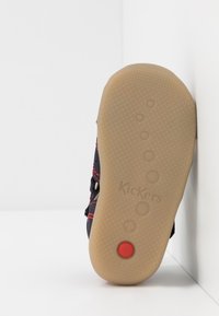 Zapato negro y rojo con una suela de goma texturizada que presenta indentaciones circulares y un acento rojo. Logo "Kickers" grabado en la parte inferior.