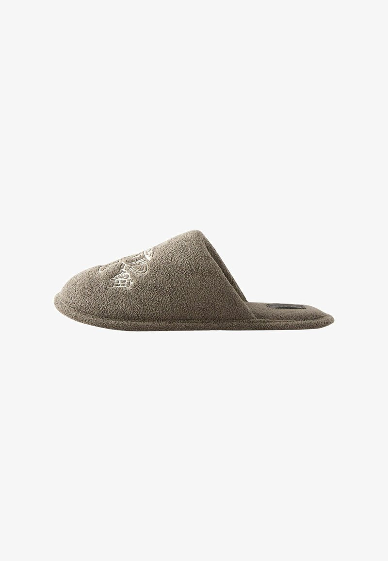 Chausson marron clair ouvert à l'arrière avec motif brodé sur le dessus, semelle plate et texture douce, conçu pour le confort intérieur.