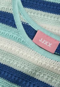 Prugasta pletenina u svijetloplavoj, mint zelenoj i mornarskoj boji. Ima mekanu teksturu, okrugli izrez i ružičastu oznaku s tekstom "JJXX".