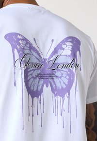Hvid bomulds t-shirt med et stort, lilla sommerfuglsgrafik på ryggen med dryppende maleeffekt og stiliseret tekst "Closure London."