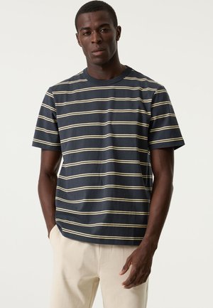 Marineblaues T-Shirt mit gelben Streifen, aus Baumwolle, mit Rundhalsausschnitt und kurzen Ärmeln, kombiniert mit hellen Hosen.