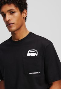 Zwarte katoenen T-shirt met een witte grafische print op de borstzak en het "KARL LAGERFELD" logo in het wit op de rand van de zak.