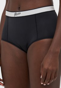 Cueca de biquíni preta de cintura alta, feita de material suave. Apresenta uma faixa elástica branca contrastante com o logótipo da Puma e detalhes de costura plana.