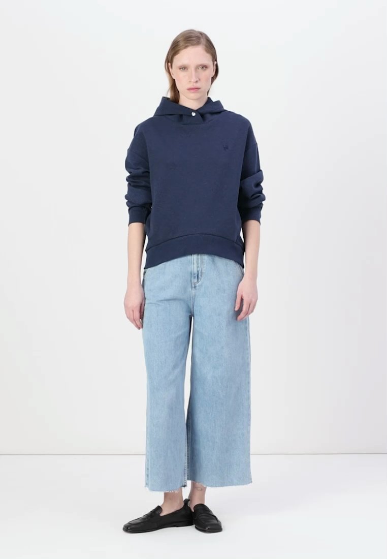 Sweat à capuche bleu marine avec un col à boutons, associé à un pantalon en denim large bleu clair et des chaussures noires à lacets.