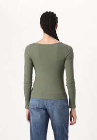 Långärmad, ribbad topp i olivgrön, med en vid halsringning och en åtsittande design, parat med blå jeans.