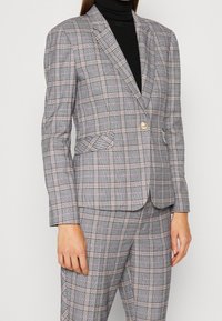 Szara marynarka w kratę o dopasowanym kroju, z różowymi i czarnymi akcentami, dwoma przednimi kieszeniami oraz pojedynczym złotym guzikiem do zapinania.