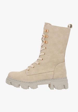 Bottines en faux suède beige à lacets avec une tige haute, bout rond et semelle en caoutchouc épaisse. Présente des œillets dorés et une languette à l'arrière.