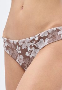 Parte inferior de bikini marrón con estampado de flores blancas. Fabricada con tela suave y con una cintura de ancho medio.